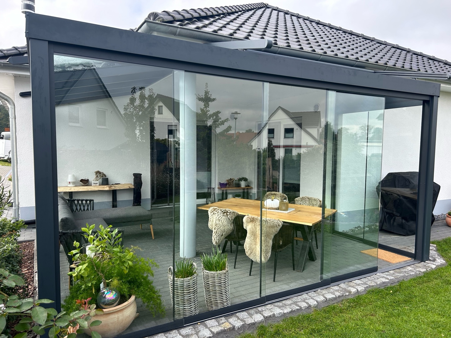 Aluminium Terrassenüberdachung in Anthrazit mit Glasdach und Glasschiebewänden über moderner Terrasse im Garten