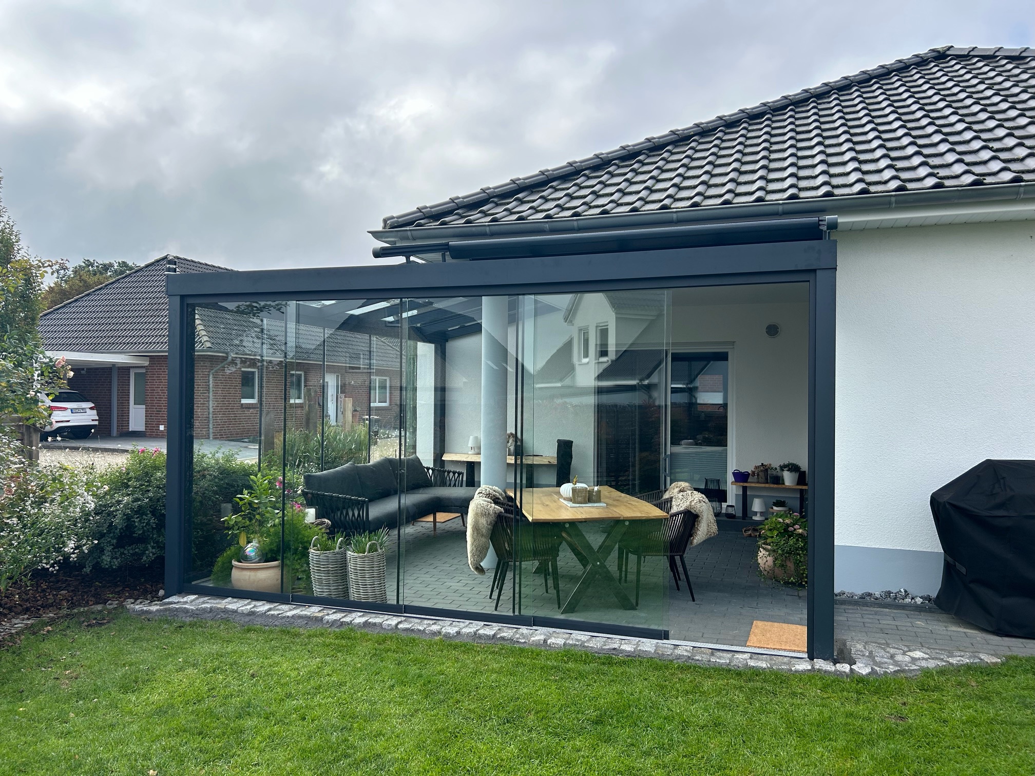 Moderne Terrassenüberdachung aus Aluminium mit Glasdach und großen Glasschiebewänden auf der Terrasse