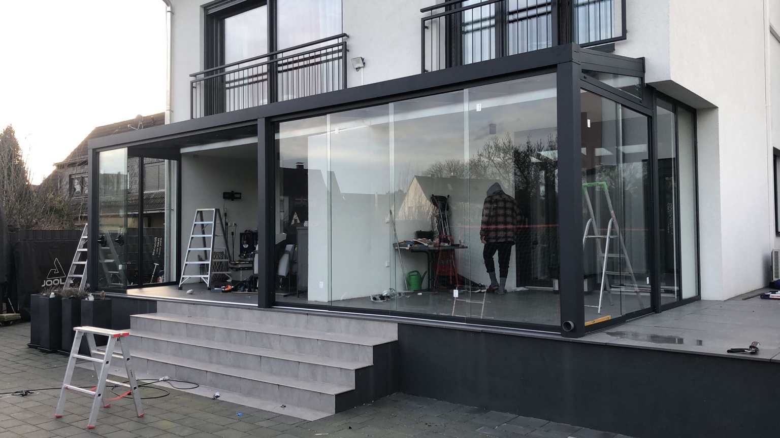 Terrassenüberdachung mit Glasdach und großen Glasschiebewänden über einer modernen Terrasse