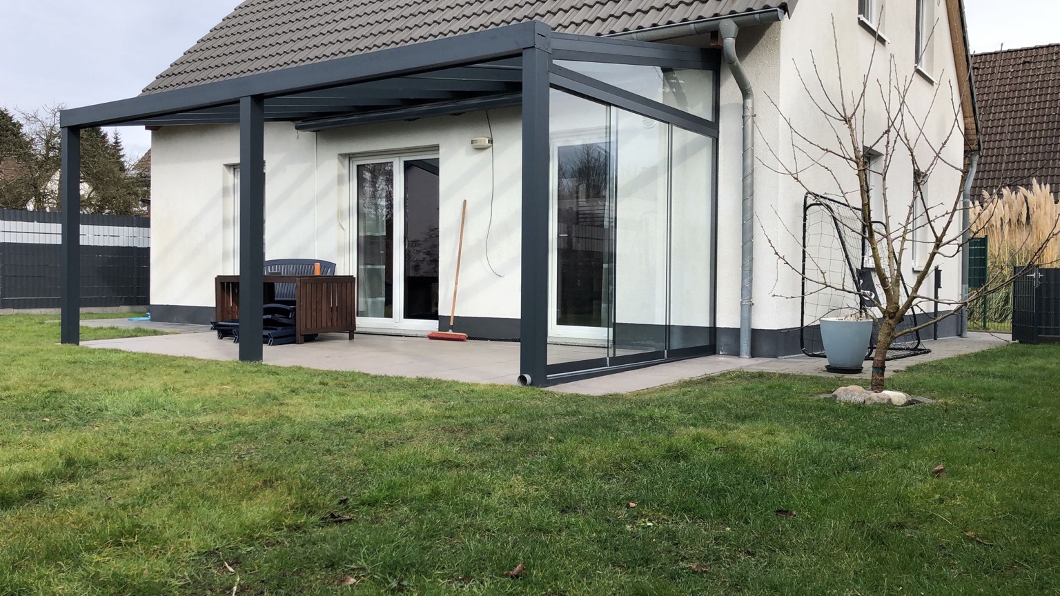 Moderne Terrassenüberdachung mit Glasdach und Glasschiebewänden an einer Hausfassade